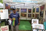 artist standing next to their work holding a ribbon