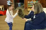 woman holding out a groundhog puppet to a young girl