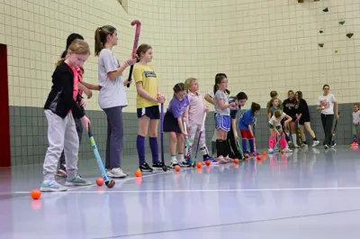 Field hockey players standing in a line on the side of the indoor court