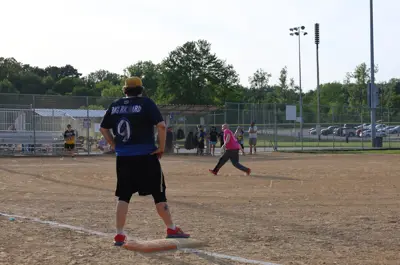 person standing on first base while another player pitches a softball