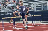 young boys running and jumping over hurdles 