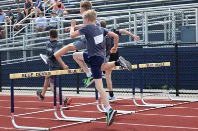 young boys running and jumping over hurdles 